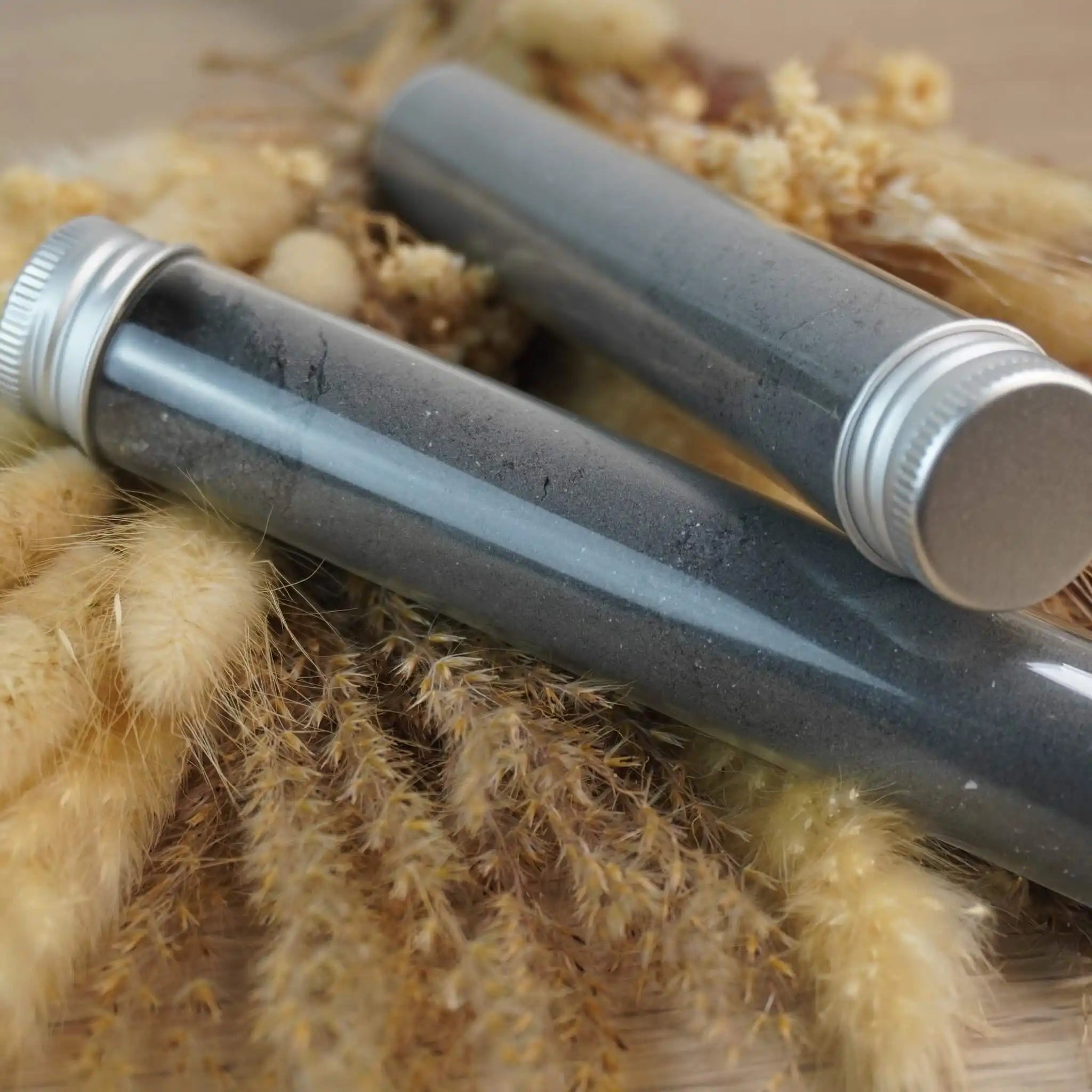 Zwei Röhrchen mit schwarzem Dekosalz auf dekorativen Getreidehalmen