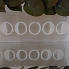 Selenit Ladeplatte mit Mondphasen Gravur zwischen grünen Blättern und Spiegelreflexion