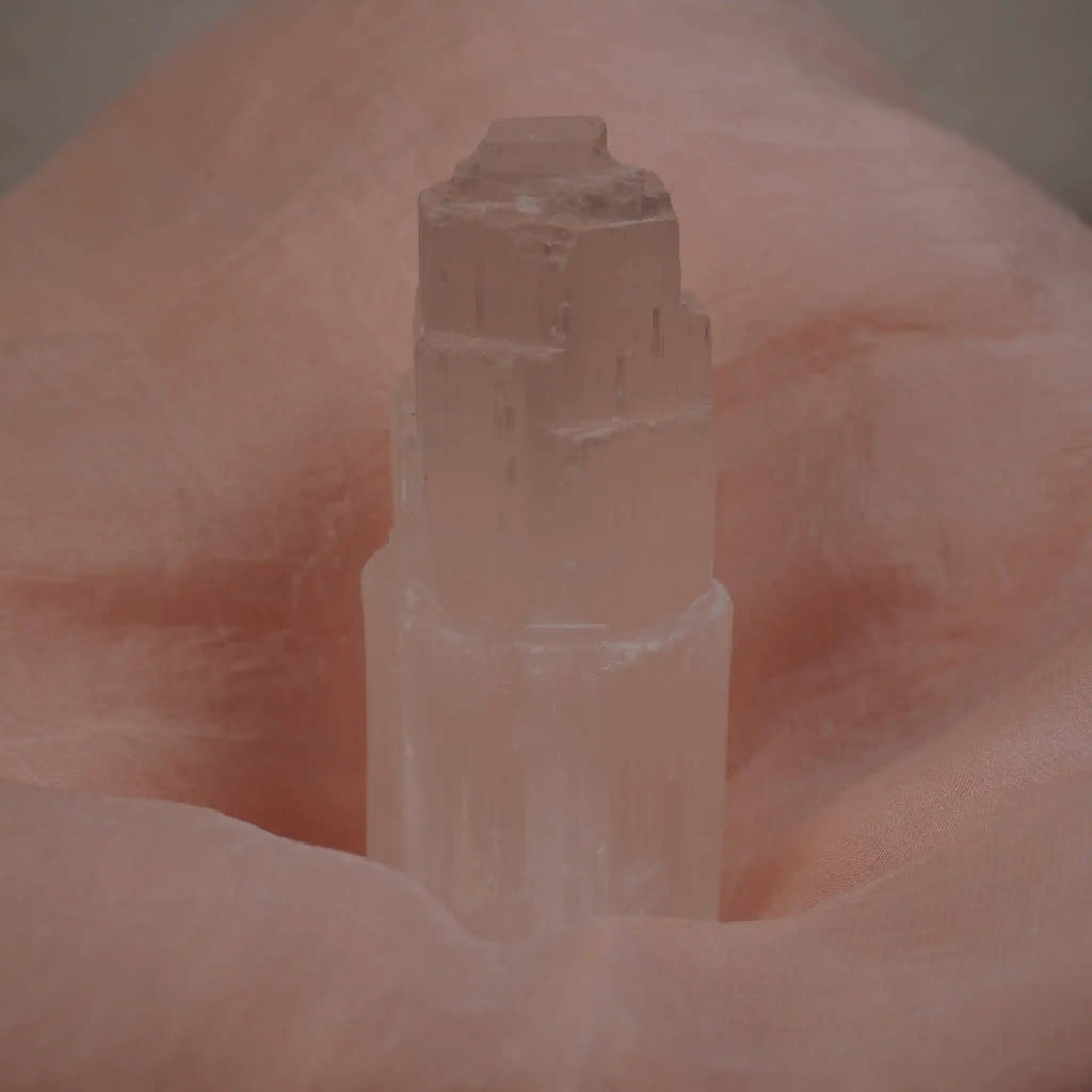 Selenit Turm Kristall vor rosa Stoffhintergrund
