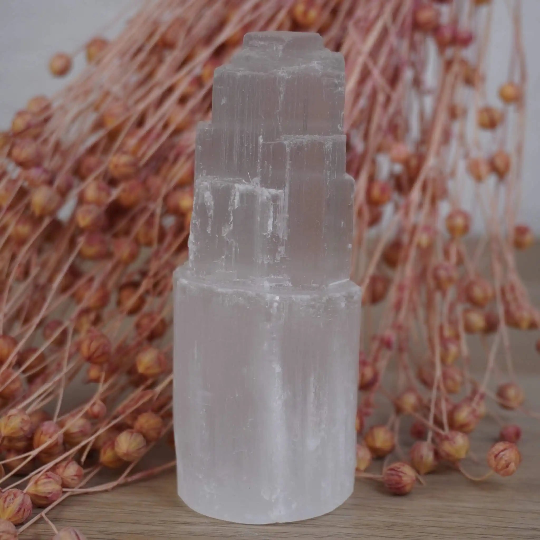 Selenit Turm Kristall vor rosa-oranger Blumendeko