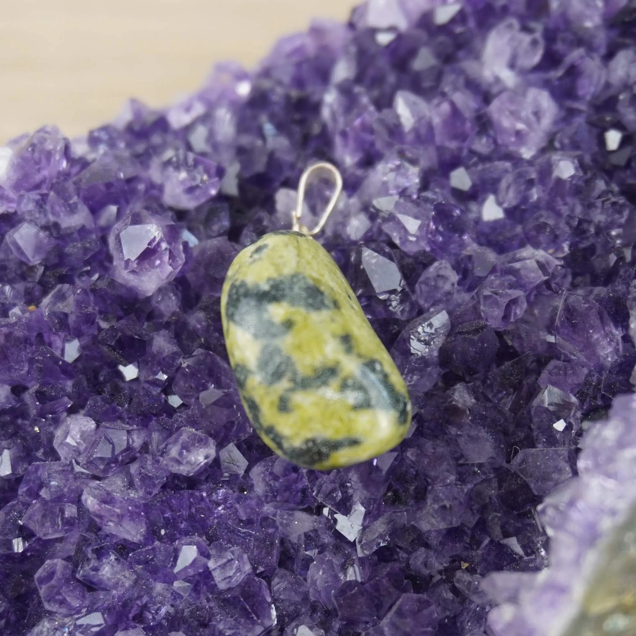 Serpentin Trommelstein Kettenanhänger mit Silber Öse auf violetter Amethyst-Druse