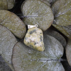 Serpentin Trommelstein Kettenanhänger mit silberfarbener Öse dekoriert auf grünen Eukalyptusblättern