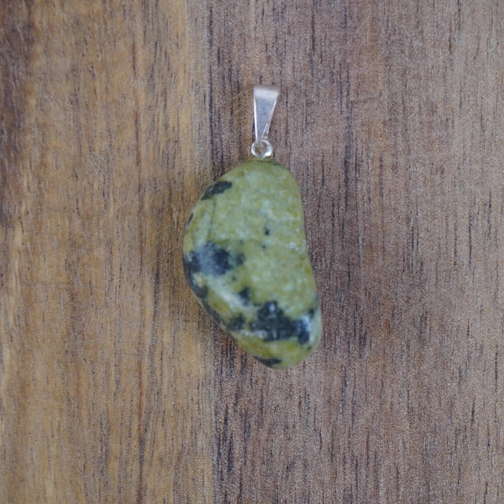 Serpentin Trommelstein Kettenanhänger mit silberfarbener Öse vor Holzuntergrund