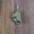 Serpentin Trommelstein Kettenanhänger mit silberfarbener Öse vor Holzuntergrund