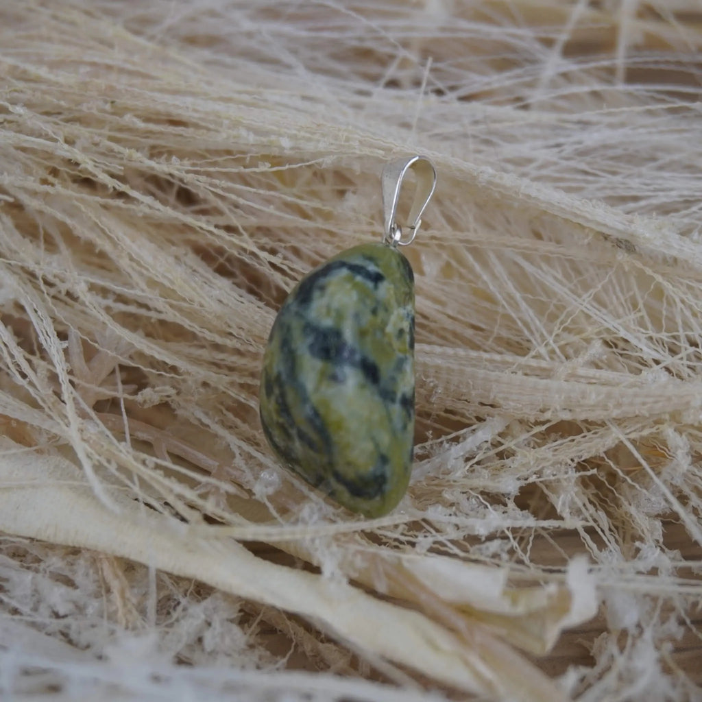 Serpentin Trommelstein Kettenanhänger mit silberner Öse auf hellen Naturfasern
