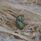 Serpentin Trommelstein Kettenanhänger mit silberner Öse auf hellen Naturfasern