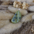 Serpentin Kettenanhänger mit silberfarbener Öse dekoriert auf beigen Trockenpflanzen