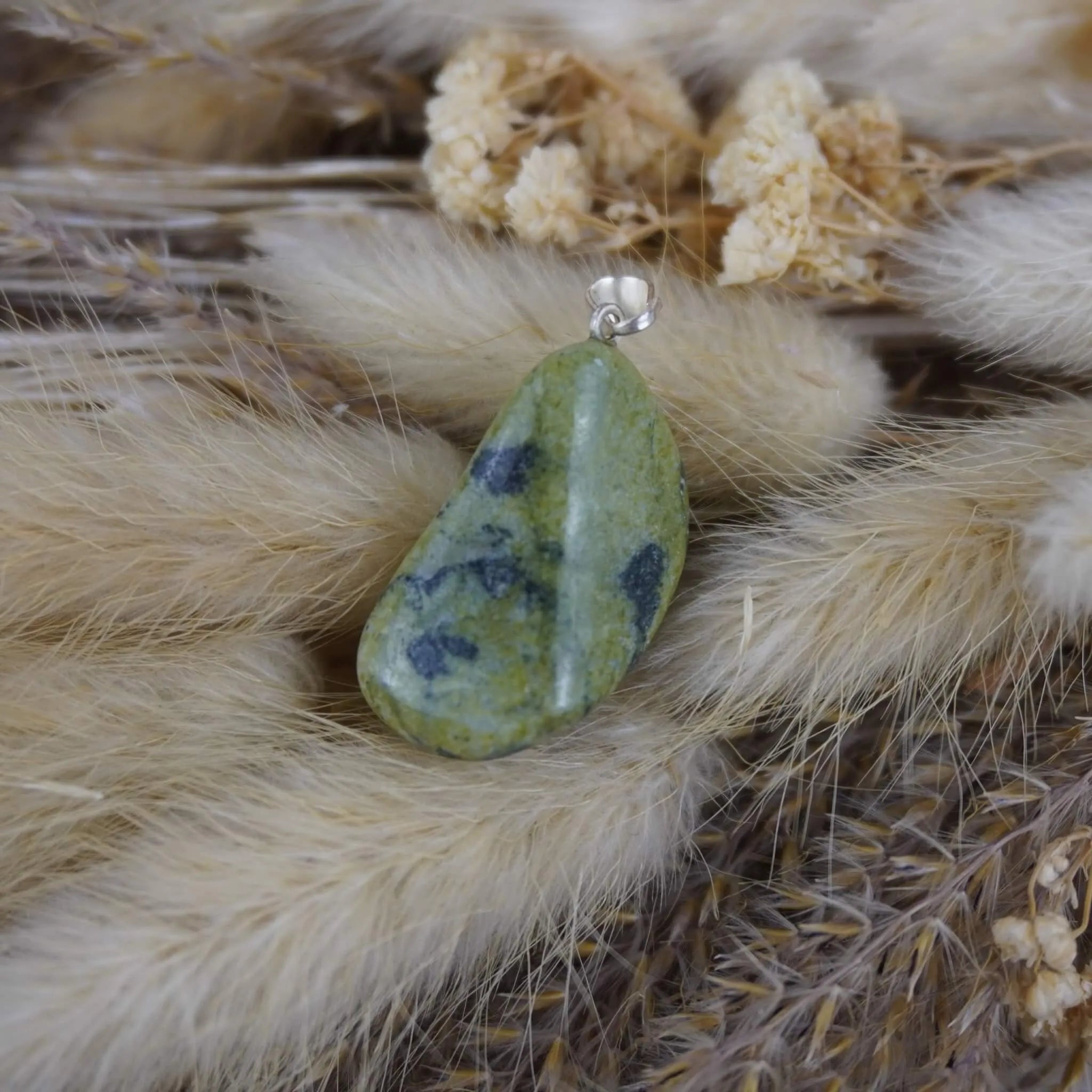 Serpentin Kettenanhänger mit silberfarbener Öse dekoriert auf beigen Trockenpflanzen