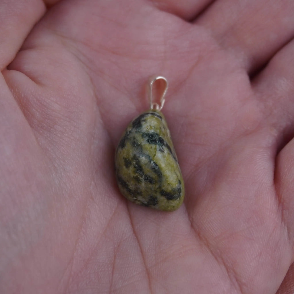 Serpentin Trommelstein Kettenanhänger mit silberner Öse in einer Hand liegend