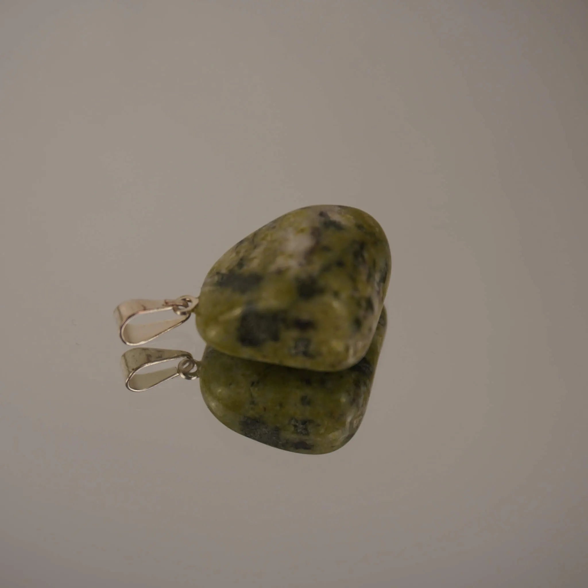 Grün gemusterter Serpentin Trommelstein Kettenanhänger mit Silber Öse auf glänzender Fläche