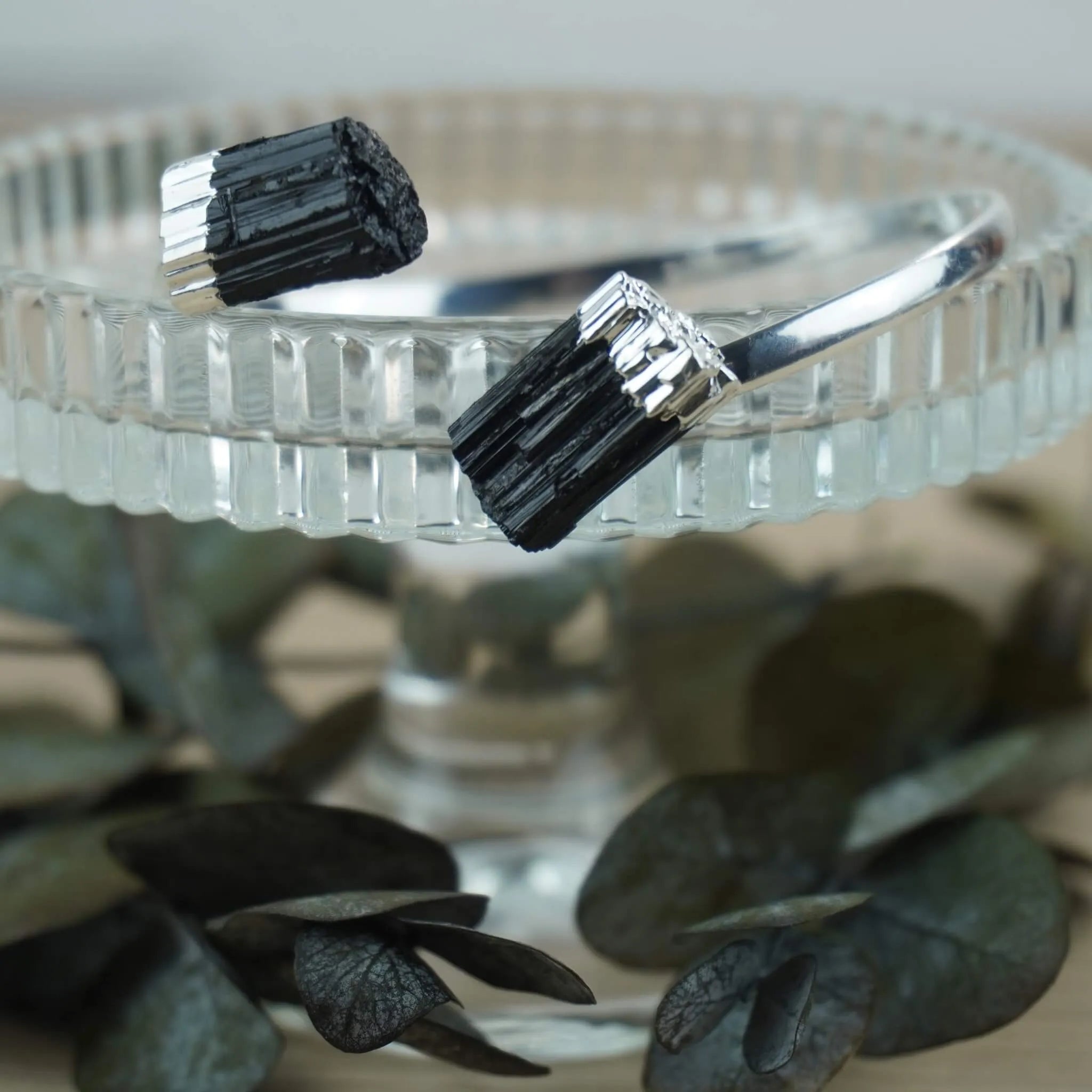 Offener Silberarmreif mit zwei schwarzen Turmalinen auf Glasständer mit Eukalyptus