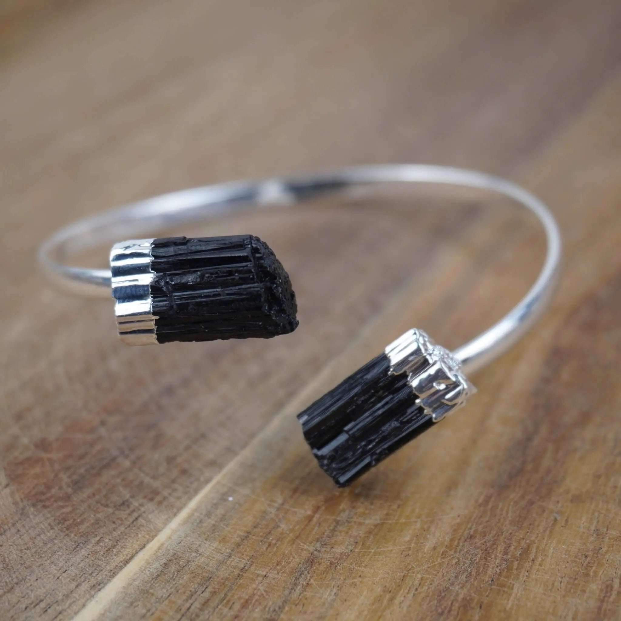 Offener Silberarmreif mit zwei schwarzen Turmalinen auf rustikaler Holzoberfläche