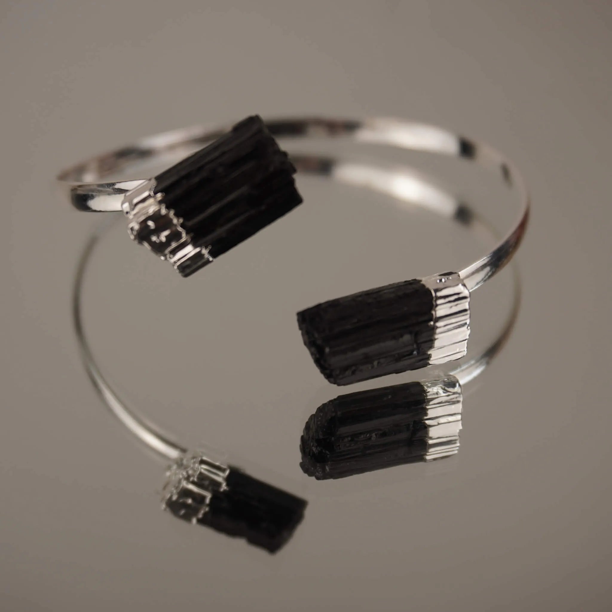Silberarmreif mit schwarzer Turmalin auf spiegelnder Fläche mit Reflexion