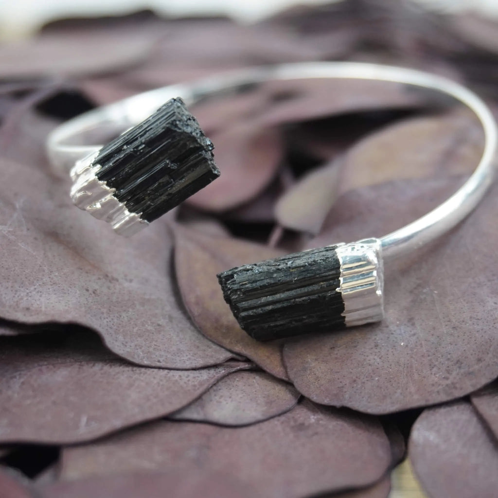 Offener Silberarmreif mit zwei rohen schwarzen Turmalinen arrangiert auf getrockneten Blättern