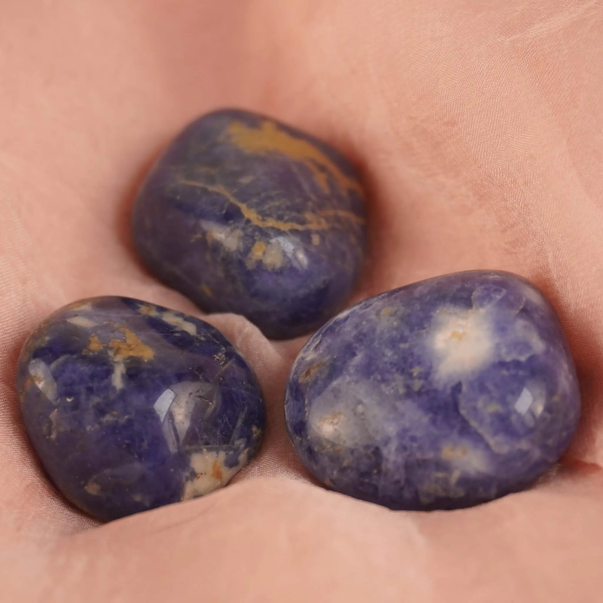 Drei Sodalith Trommelsteine auf weichem rosa Untergrund dekorativ arrangiert