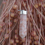 Sonnenstein Spitze Kettenanhänger mit silberfarbener Fassung vor rosa Trockenblumen