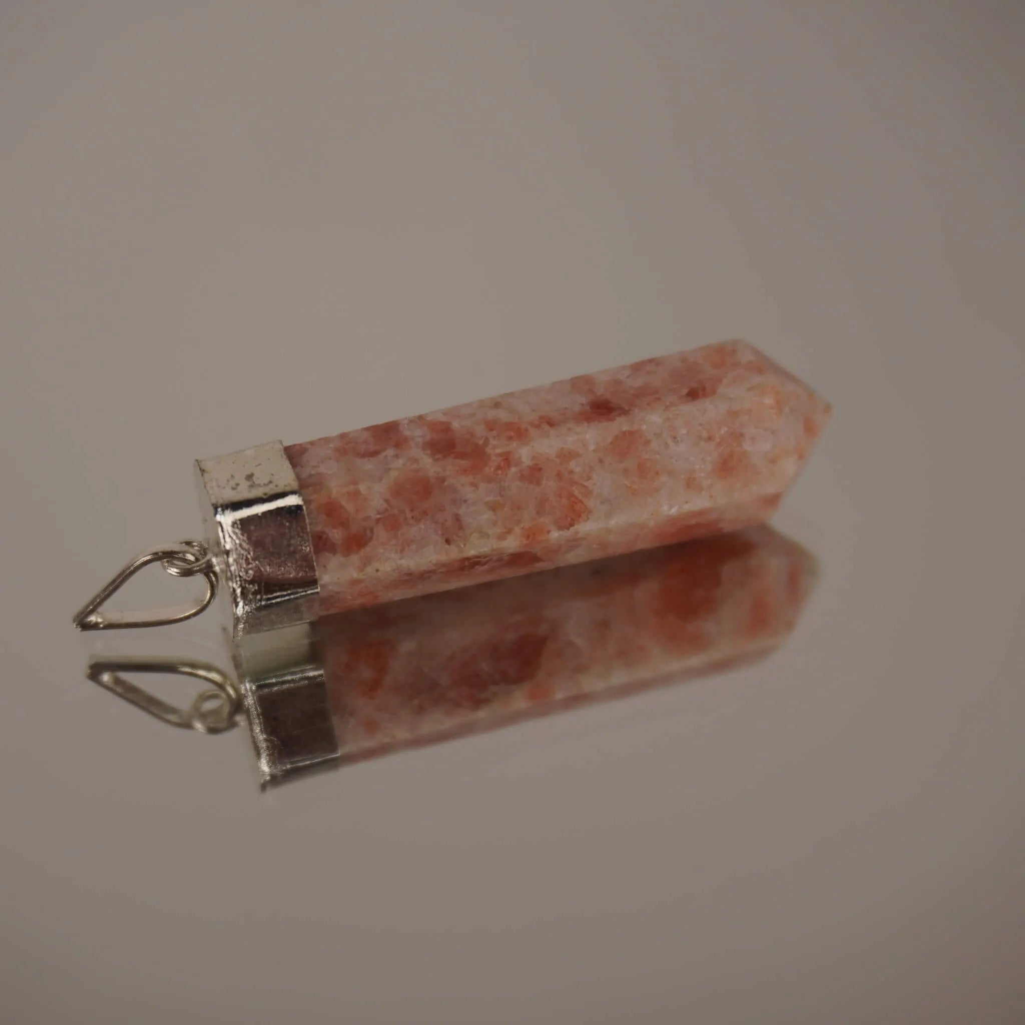 Liegender Sonnenstein Spitze Kettenanhänger mit silberfarbener Fassung und Spiegelung auf glänzender Fläche