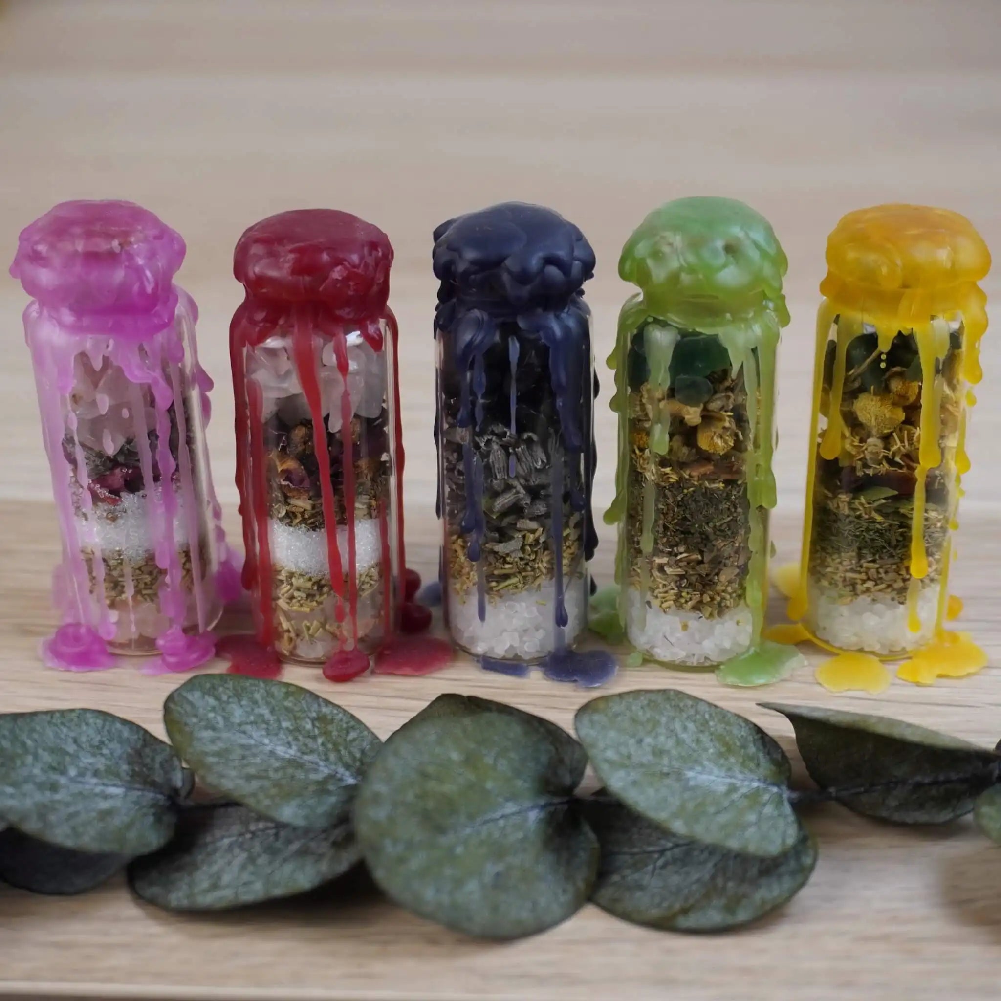 Spell Jar Set aus fünf handgefertigten Gläsern mit buntem Wachs in lila, rot, blau, grün und gelb, gefüllt mit Kristallen und Kräutern