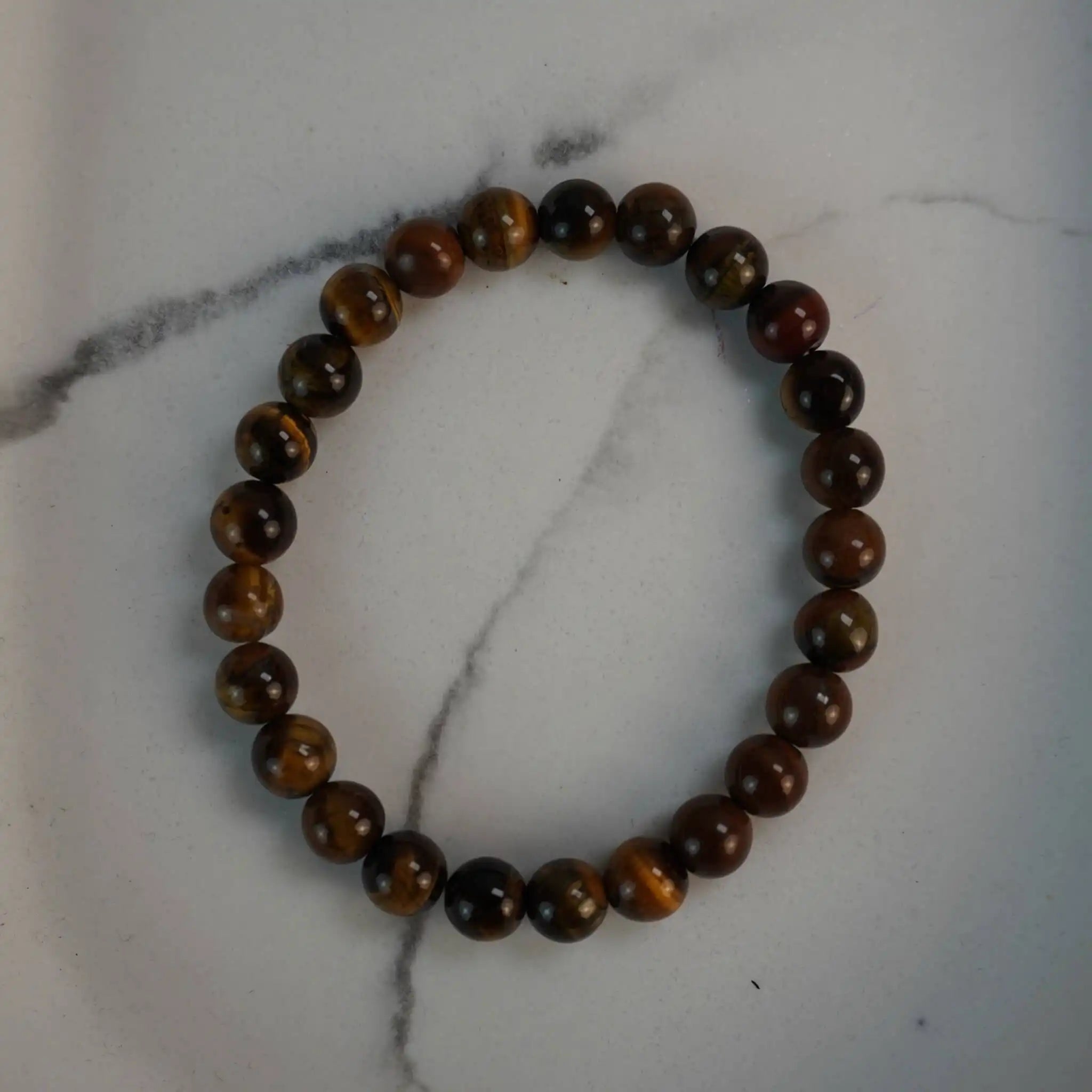 Tigerauge Kugelarmband aus polierten Perlen auf weißem Marmor-Hintergrund