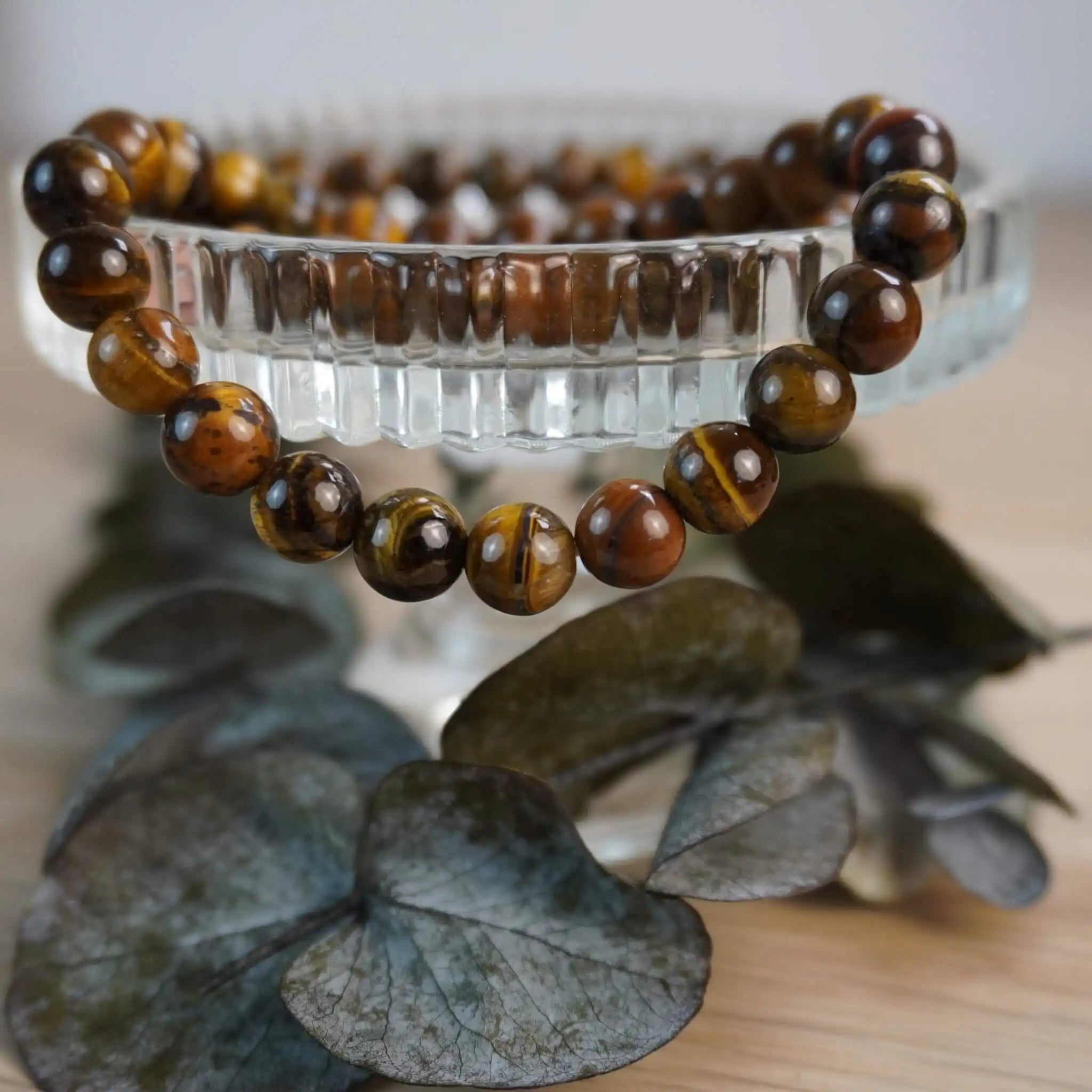 Tigerauge Kugelarmband auf dekorativer Glasvase mit Blättern