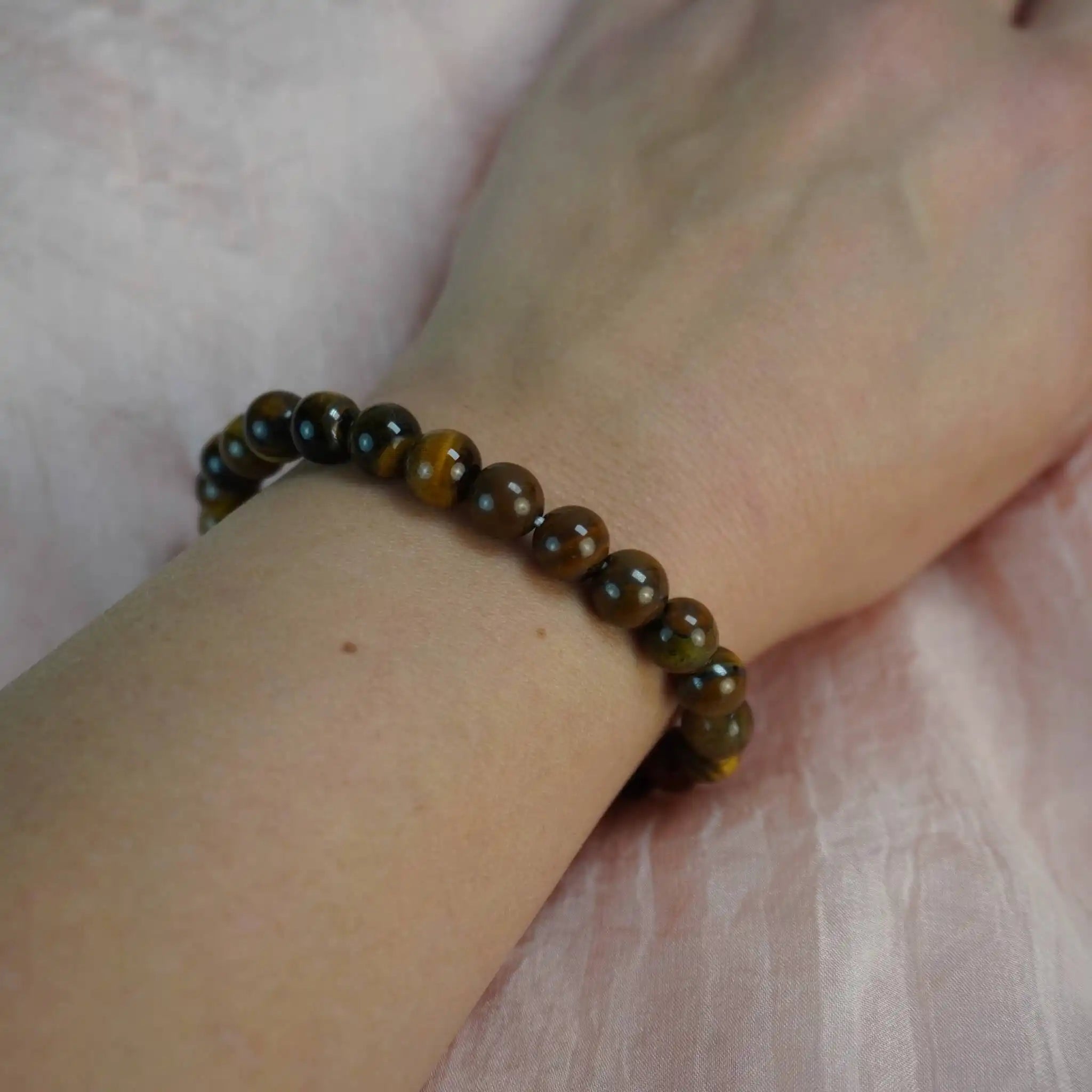 Tigerauge Kugelarmband getragen am Handgelenk auf rosa Stoff