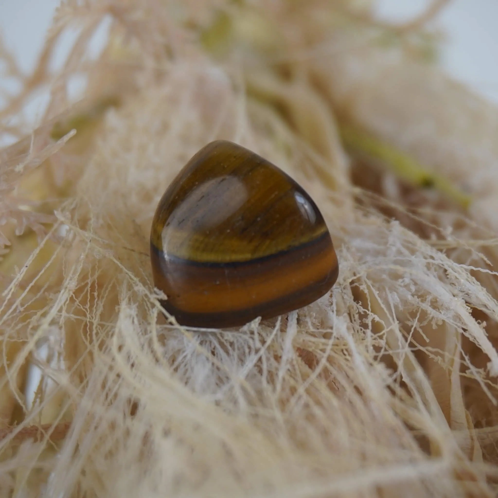 Tigerauge Trommelstein auf hellen Naturfasern mit warmem Goldbraun