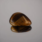 Tigerauge Trommelstein mit Spiegelung auf glänzender Oberfläche in Nahaufnahme