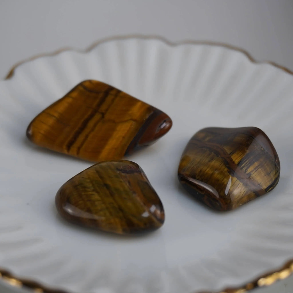 Drei Tigerauge Trommelsteine auf weißem Teller mit Goldrand dekorativ arrangiert