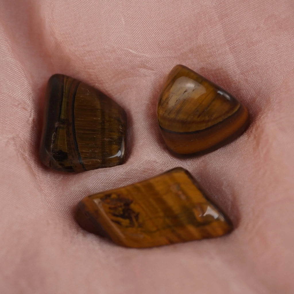 Drei Tigerauge Trommelsteine auf rosa Stoff weich gebettet