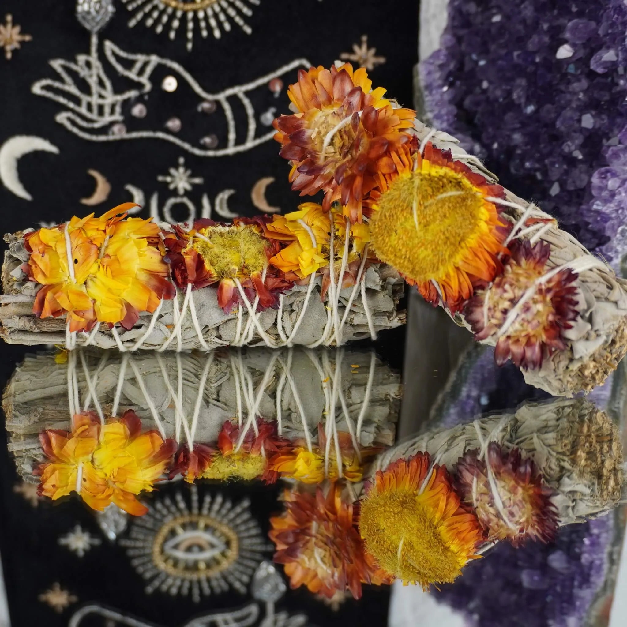 Weißer Salbei Räucherbündel mit orangegelben Blüten vor spirituellem Hintergrund und Amethyst-Druse arrangiert