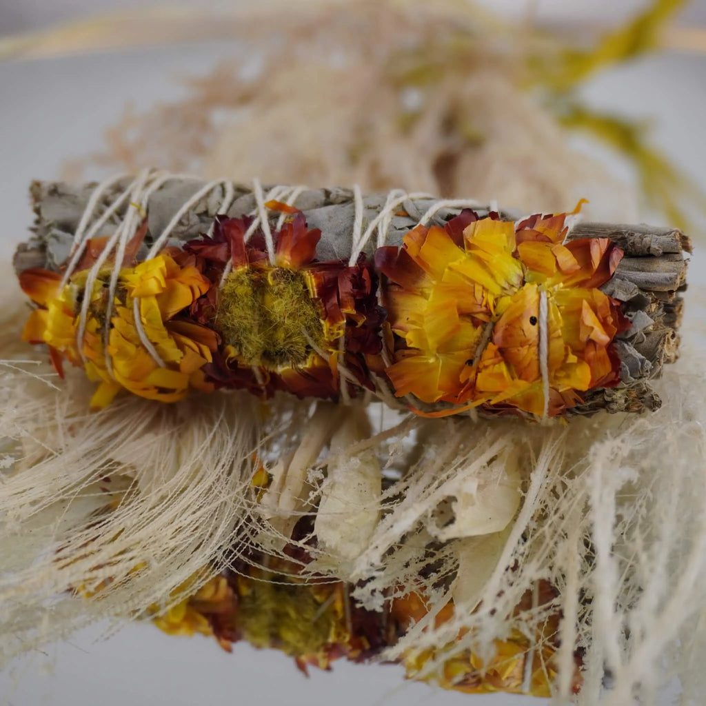Weißer Salbei Räucherbündel mit gelben und roten Siempreviva Blüten vor naturfarbenen Trockenpflanzen
