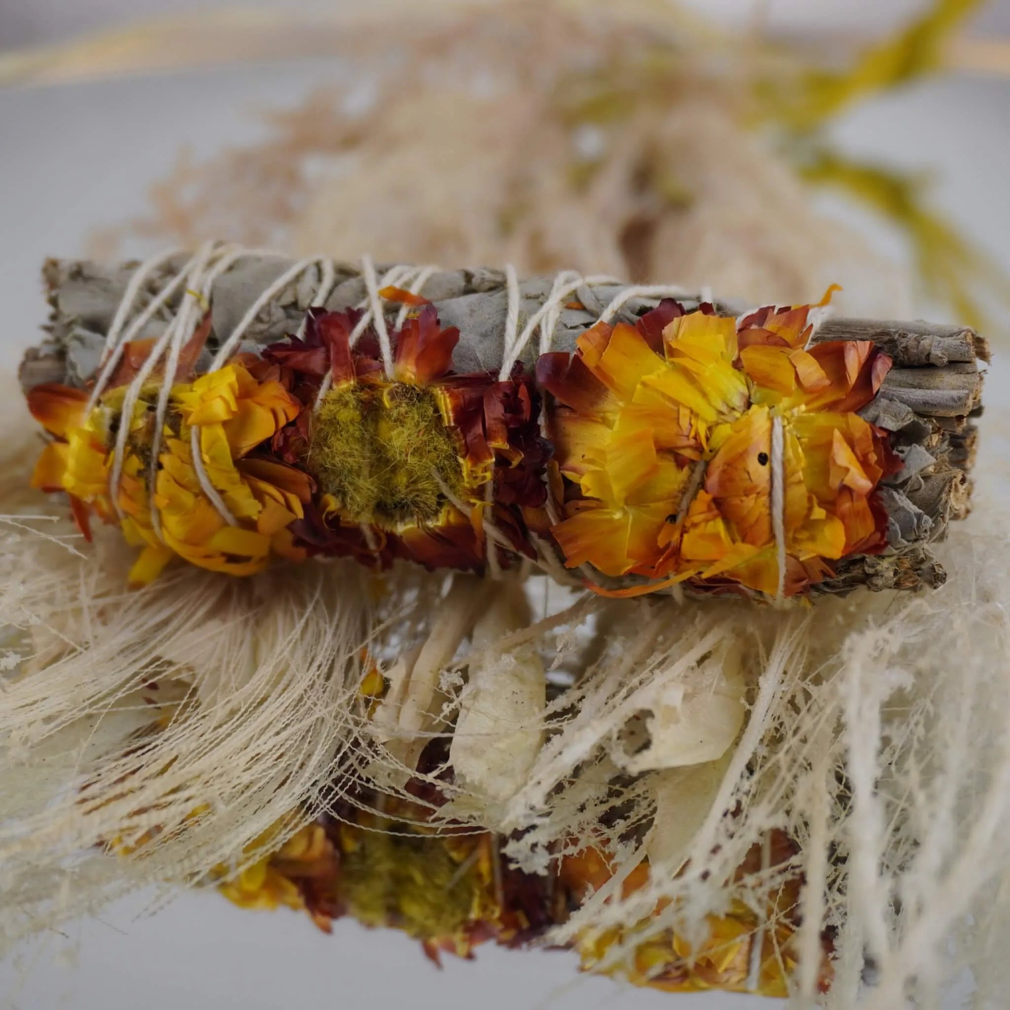 Weißer Salbei Räucherbündel mit gelben und roten Siempreviva Blüten vor naturfarbenen Trockenpflanzen