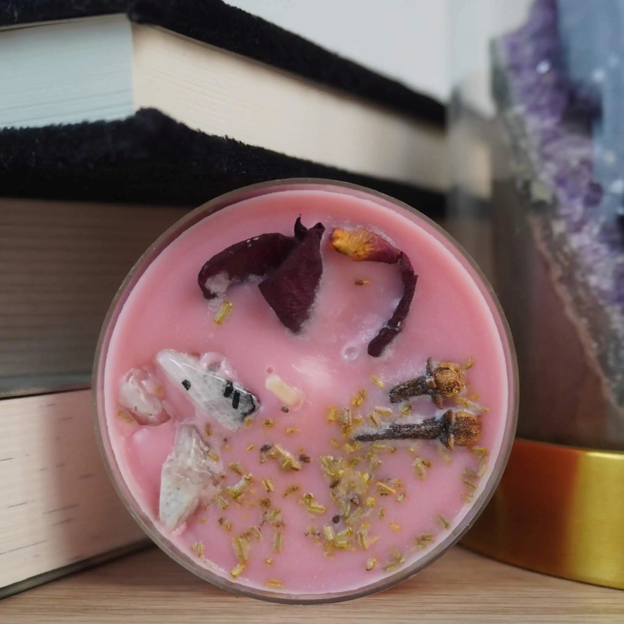 Maxi-Teelicht mit Zimtduft und Mondstein, verziert mit Blüten und Kräutern, arrangiert zwischen Büchern und Kristallen